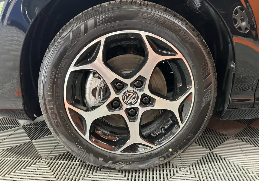 Gros plan sur la roue avant gauche du MG3 Hybrid+ 195 Luxury Pebble Black avec jante alliage bicolore et logo MG central.