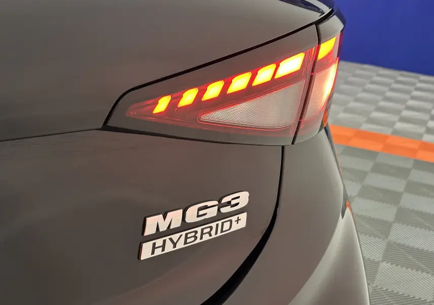 Gros plan sur le feu arrière droit allumé et le logo MG3 Hybrid+ sur la carrosserie Pebble Black.