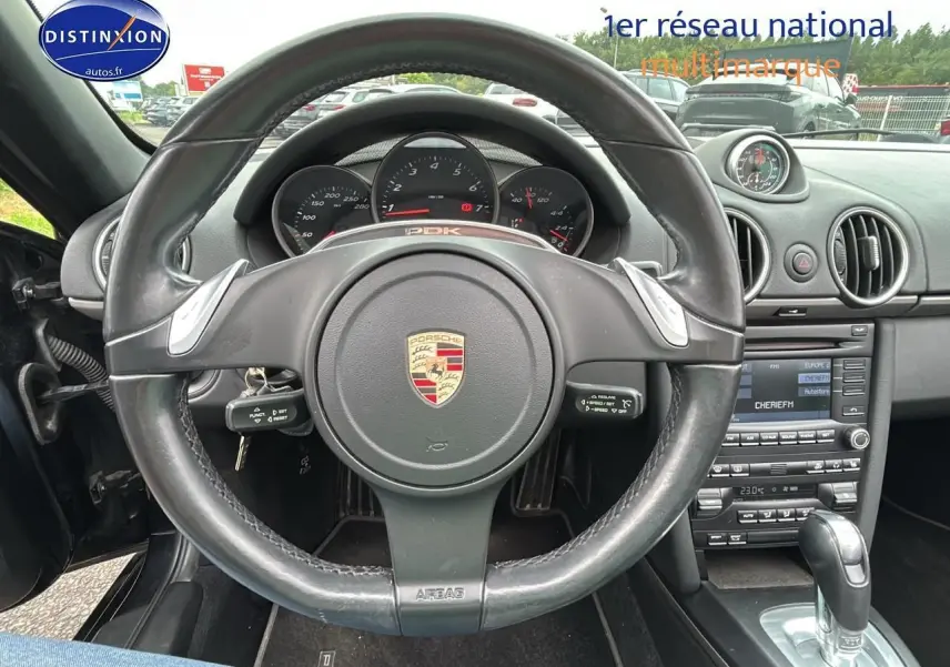 Vue rapprochée du volant cuir noir et du tableau de bord de la Porsche Boxster 987 2.9 PDK de 2012.