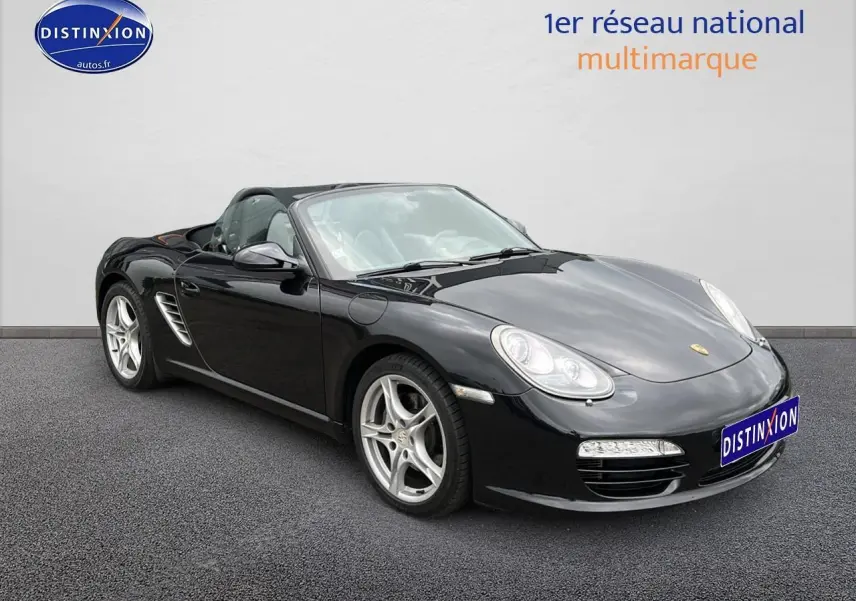 Porsche Boxster 987 noir vue 3/4 avant droit, capote ouverte et jantes alu 17 pouces visibles.