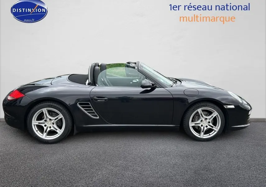 Profil côté gauche d'une Porsche Boxster 987 noire cabriolet, avec jantes alu 17 pouces et capote ouverte.