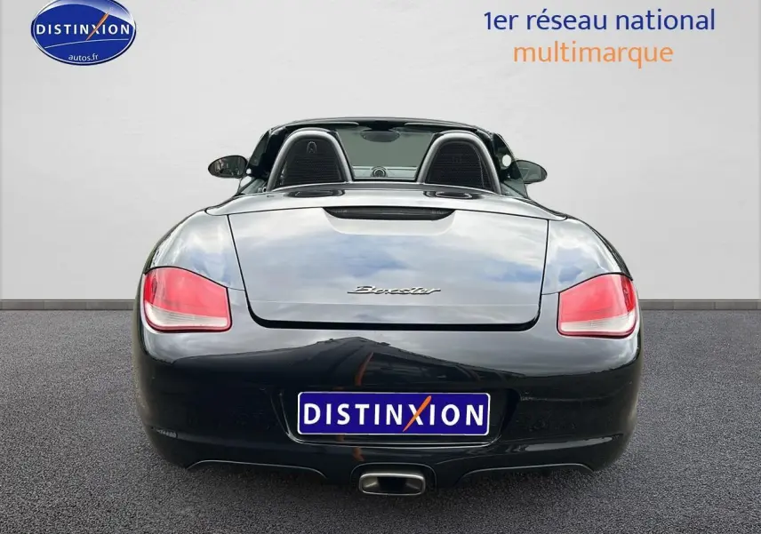 Vue arrière d'une Porsche Boxster 987 noire découvrable avec feux arrière rouges et échappement central.