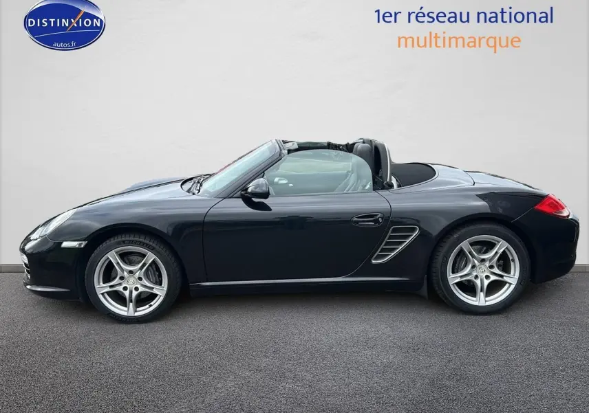 Profil côté gauche d'une Porsche Boxster 987 noire cabriolet avec jantes alu 17 pouces sur fond clair.