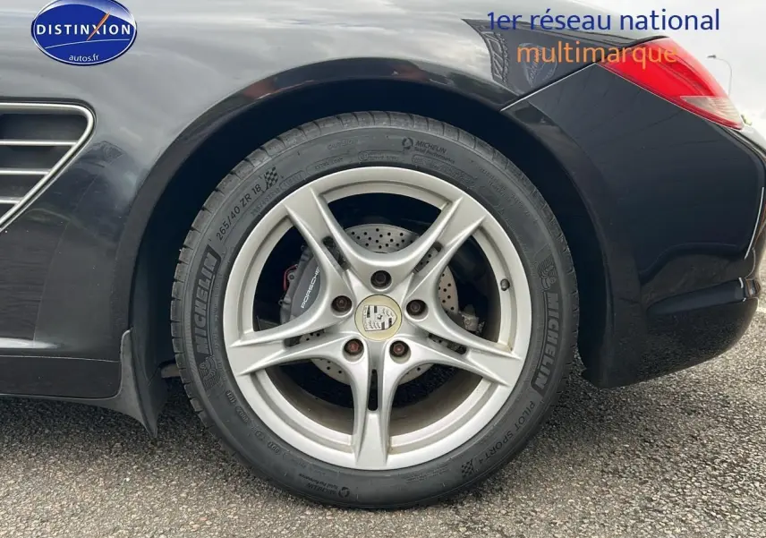 Gros plan sur la jante alu 17 pouces côté arrière droit d'une Porsche Boxster noire avec logo Porsche visible.