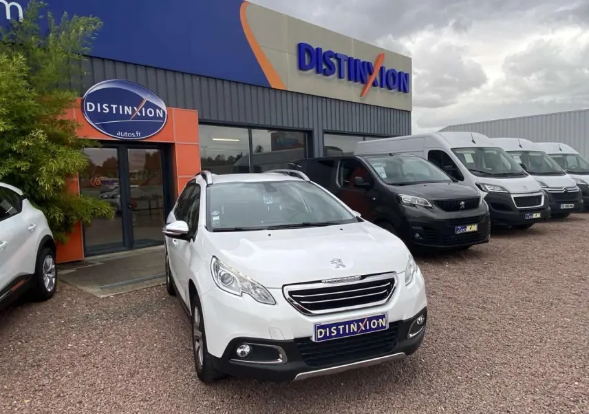 Peugeot 2008 blanc en 3/4 avant droit devant un concessionnaire Distinxion sous un ciel nuageux.