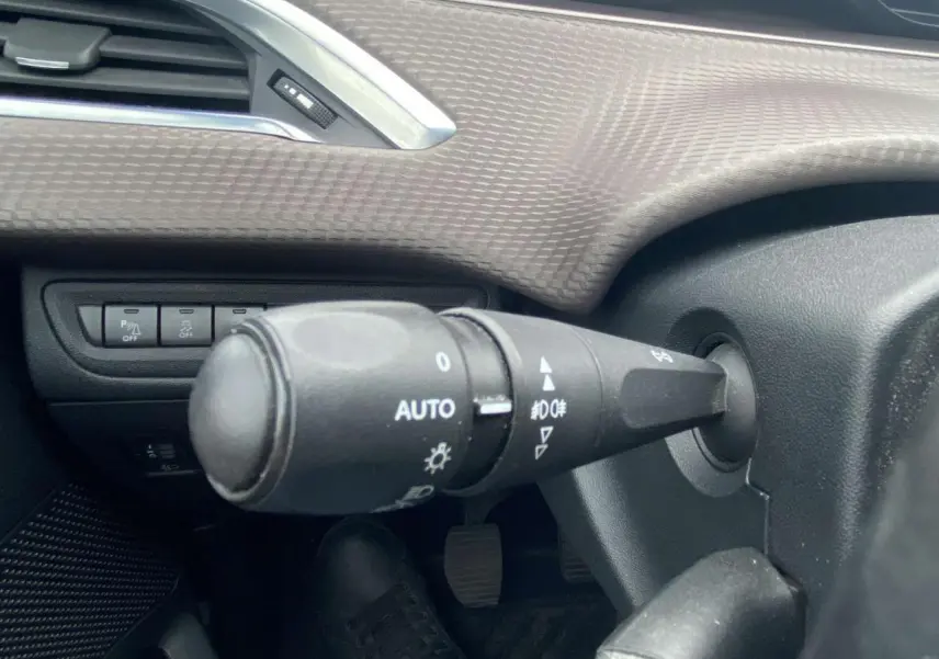 Gros plan sur la commande d'éclairage à gauche du volant dans l'habitacle du Peugeot 2008 blanc de 2015.