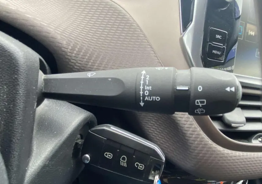 Gros plan sur la manette d'essuie-glace et le bouton de verrouillage du Peugeot 2008 blanc, intérieur côté conducteur.