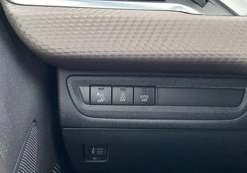 Gros plan sur les commandes de désactivation d'assistance et d'économie d'énergie dans l'habitacle d'une Peugeot 2008 blanche de 2015.
