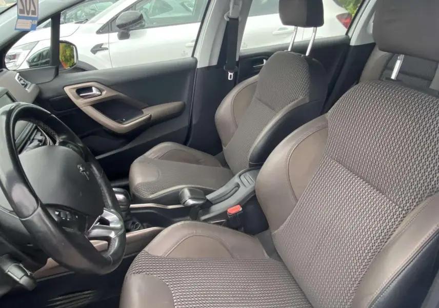 Vue intérieure côté conducteur du Peugeot 2008 blanc de 2015, avec sièges tissu et cuir gris et volant multifonction.