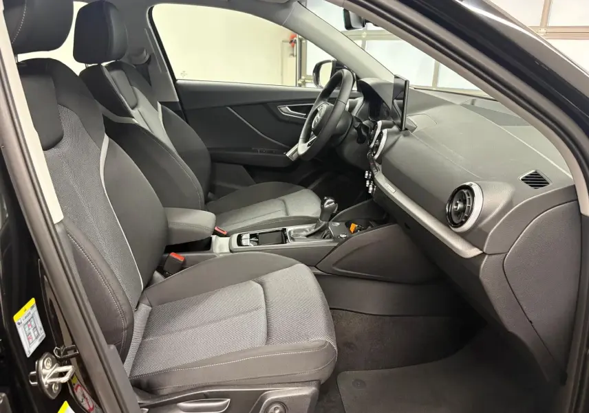 Intérieur avant droit de l’Audi Q2 35 TFSI S Line 2026 avec sièges tissu gris et tableau de bord noir.
