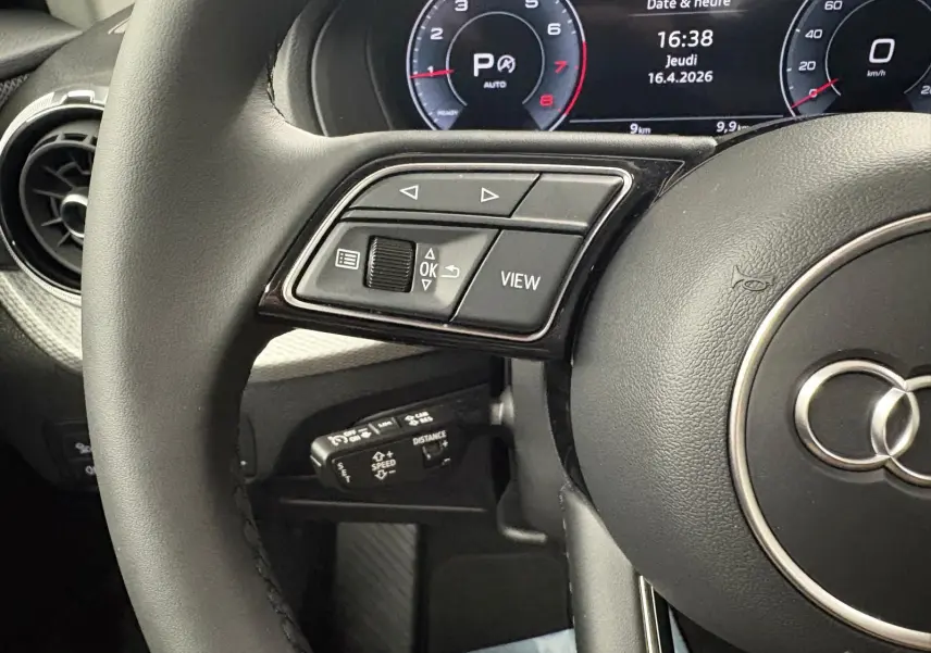 Gros plan sur le volant et le tableau de bord numérique de l’Audi Q2 35 TFSI 150 S tronic 7 S line noir mythic, affichage date et heure.