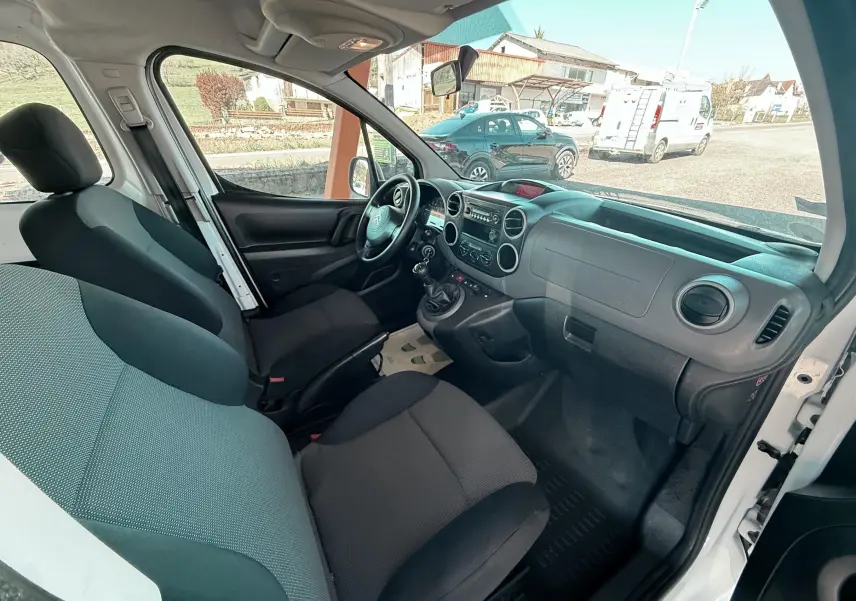 Vue intérieure côté conducteur du Citroën Berlingo blanc 2017, montrant le tableau de bord et les sièges en tissu noir.