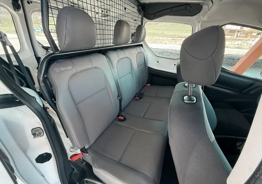 Vue intérieure côté droit du Citroën Berlingo blanc, montrant la banquette arrière grise avec séparation grillagée.
