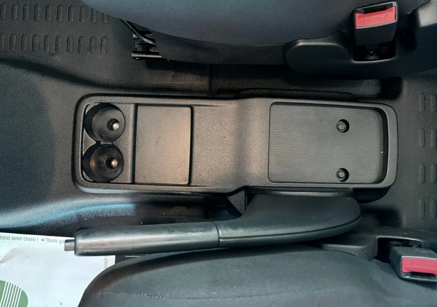 Vue plongeante sur la console centrale noire du Citroën Berlingo blanc, avec frein à main et porte-gobelets visibles entre les sièges.