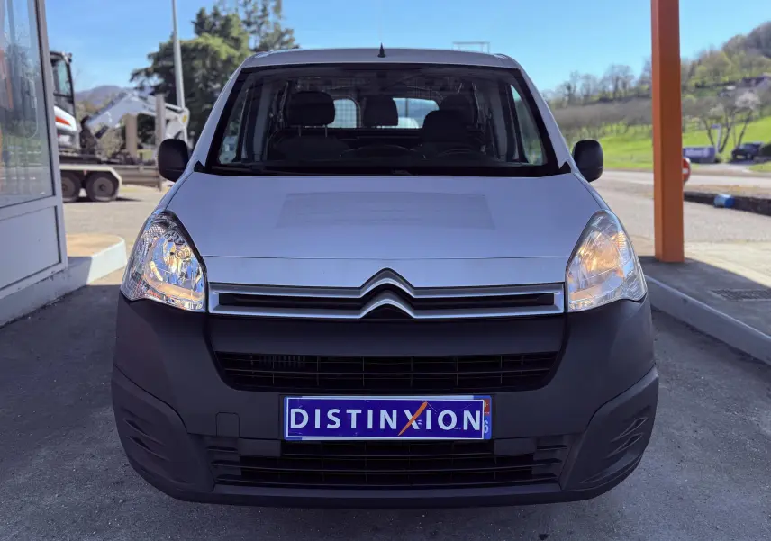 Vue frontale d’un Citroën Berlingo blanc avec phares allumés et pare-chocs noir mat sous un abri.