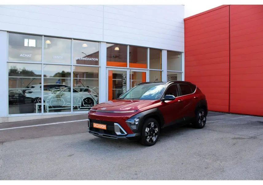 Hyundai Kona 2024 rouge Ultimate Metal avec toit noir, vu en 3/4 avant droit devant un bâtiment commercial.