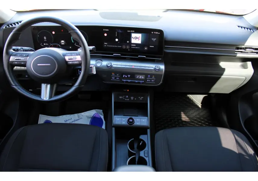 Vue intérieure avant du tableau de bord et volant cuir noir du Hyundai Kona 2024 avec écran tactile panoramique et console centrale.