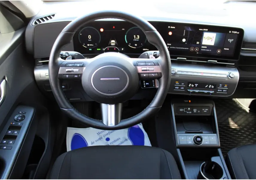 Vue intérieure frontale du tableau de bord et volant cuir noir du Hyundai Kona 2024, avec écran tactile panoramique.