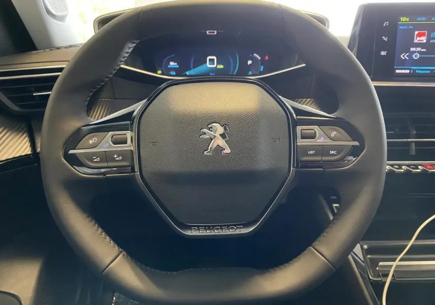 Vue rapprochée du volant cuir noir du Peugeot 2008 e-136 Allure Pack 2022 avec commandes intégrées et tableau de bord numérique.