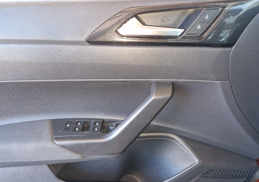 Vue intérieure côté conducteur de la porte d'une Volkswagen Taigo rouge roi 2023 avec commandes de vitres et verrouillage.