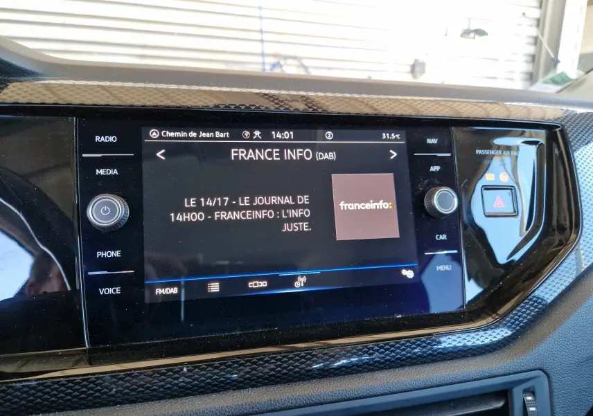 Écran tactile central du Volkswagen Taigo 2023 affichant la radio France Info avec commandes autour et finition noire brillante.