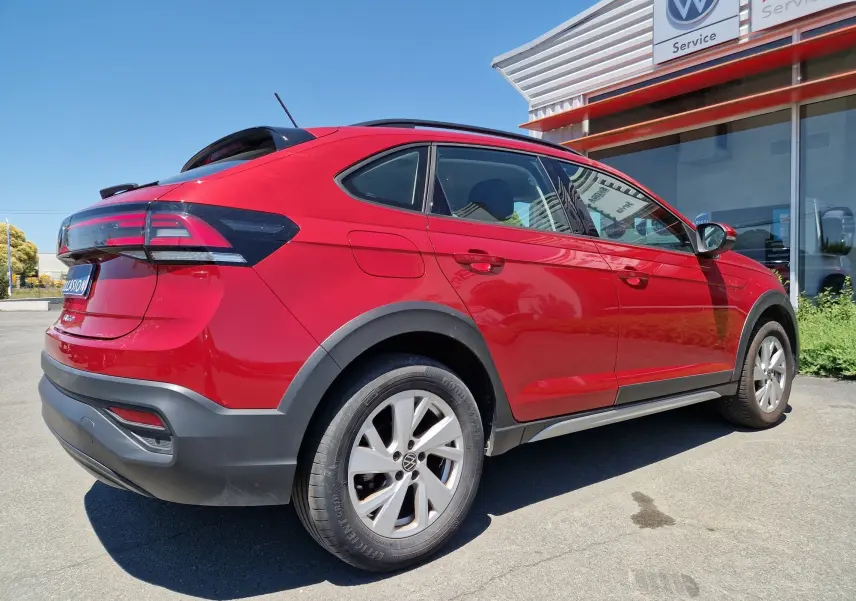 Vue 3/4 arrière droite d'un Volkswagen Taigo rouge roi garé devant un service Volkswagen avec ses feux arrière distinctifs.
