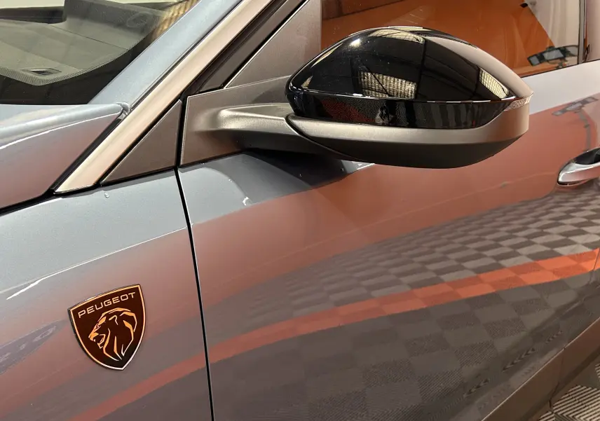 Gros plan sur le côté gauche bleu Ingaro du Peugeot 5008 III Hybrid avec rétroviseur noir brillant et logo lion.