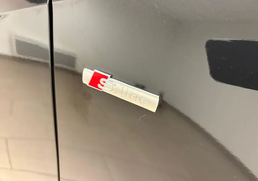 Gros plan sur l'emblème S line argent et rouge sur la carrosserie noire métallisée d'un Audi Q2.