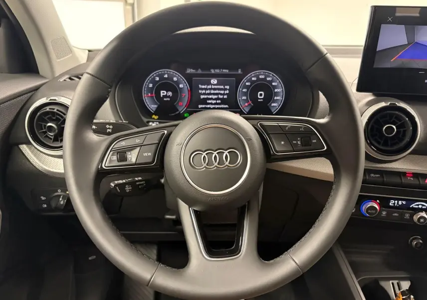Vue rapprochée du volant multifonction noir de l'Audi Q2 35 TFSI S Line avec tableau de bord numérique allumé.