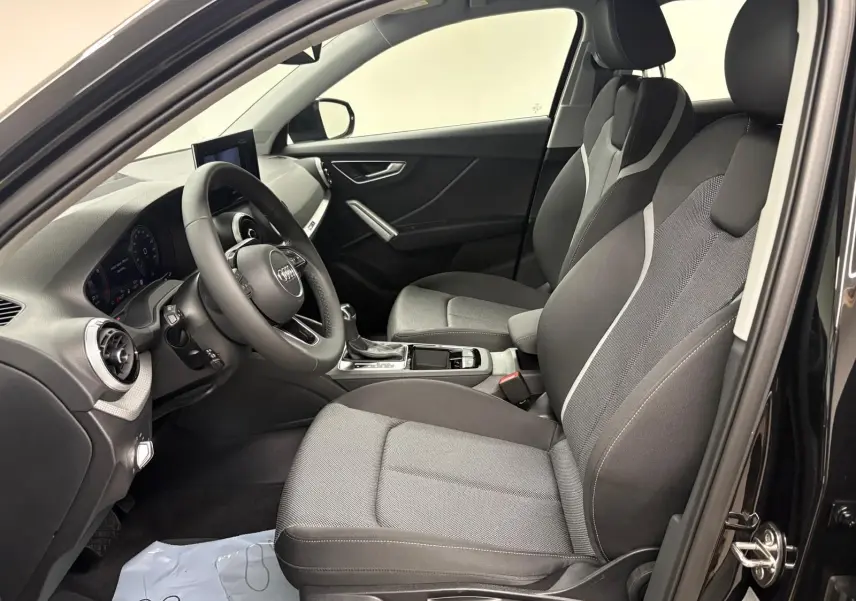 Vue intérieure côté gauche de l'Audi Q2 35 TFSI S Line 2026 avec sièges tissu gris et tableau de bord noir.