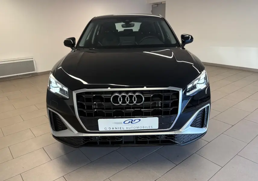Vue avant d'un Audi Q2 35 TFSI S Line noir mythic avec calandre large et phares LED allumés en intérieur showroom.