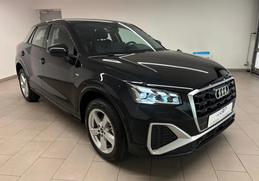 Audi Q2 35 TFSI S Line noir mythic en 3/4 avant droit, avec calandre hexagonale et phares LED allumés.