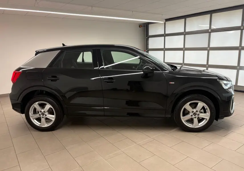 Audi Q2 35 TFSI S Line noir mythic vue de profil côté gauche dans un garage lumineux, jantes alliage visibles.