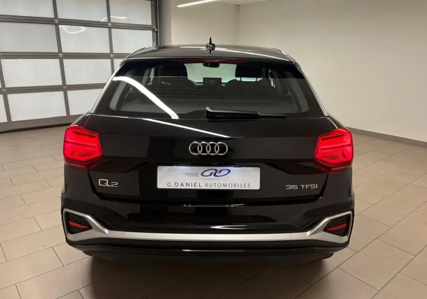 Vue arrière d'un Audi Q2 35 TFSI noir mythic, avec feux rouges allumés et détails chromés sur le pare-chocs.