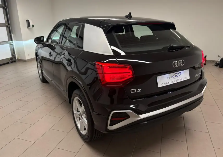 Vue 3/4 arrière droite d'un Audi Q2 35 TFSI S Line noir Mythic avec toit contrastant et feux arrière allumés.
