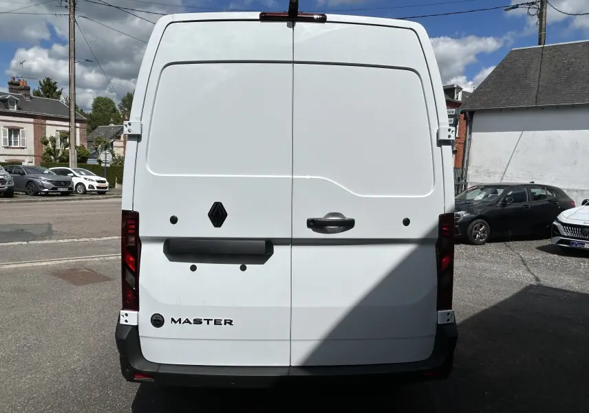 Vue arrière d’un utilitaire Renault Master blanc, avec portes battantes fermées et feux arrière verticaux rouges.