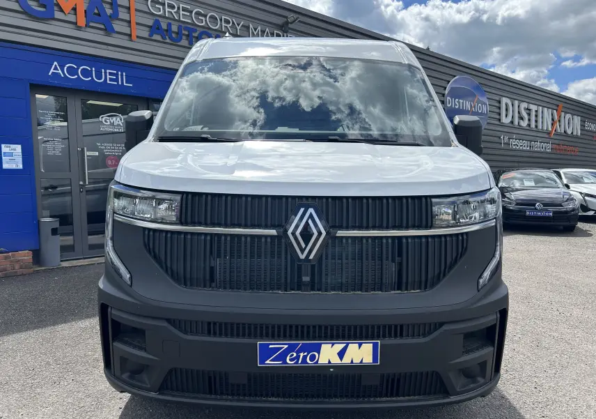 Vue frontale d’un Renault Master blanc 2025 avec calandre noire et logo Renault bien visible, stationné devant un garage.