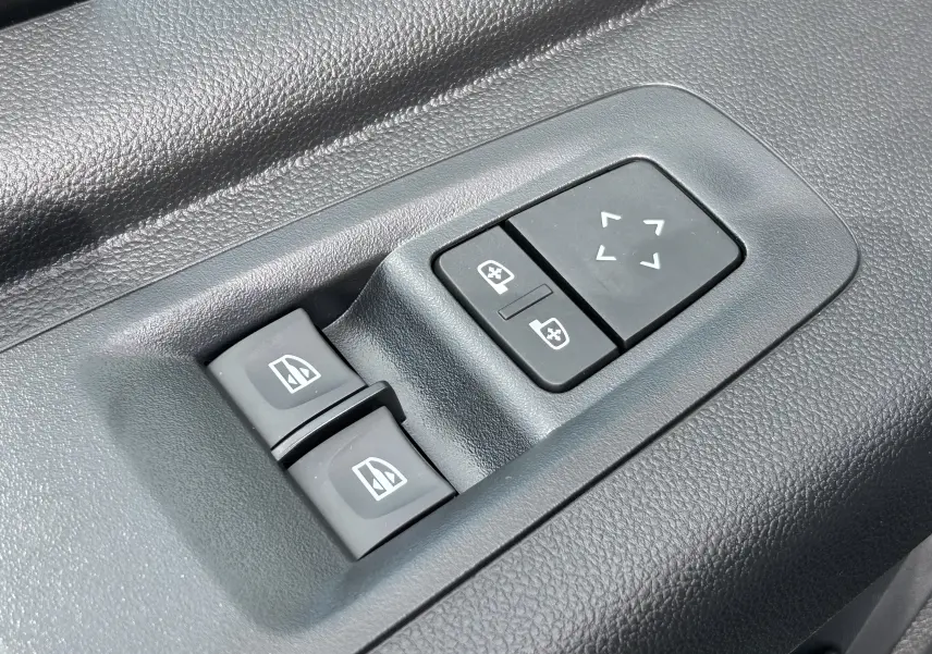 Gros plan sur les commandes électriques des vitres et des rétroviseurs sur la porte intérieure noire du Renault Master blanc.