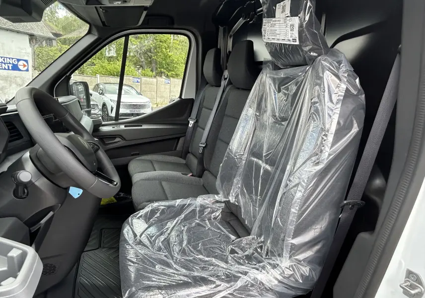 Vue intérieure côté conducteur du Renault Master blanc 2025, sièges avant en tissu protégés par film plastique.