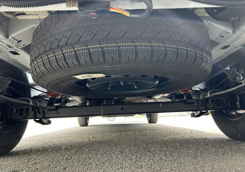 Vue en contre-plongée sous un Renault Master blanc montrant la roue de secours suspendue sous le châssis arrière.