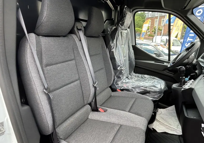Vue intérieure côté conducteur du Renault Master blanc 2025, sièges tissu gris avec siège passager protégé par housse plastique.