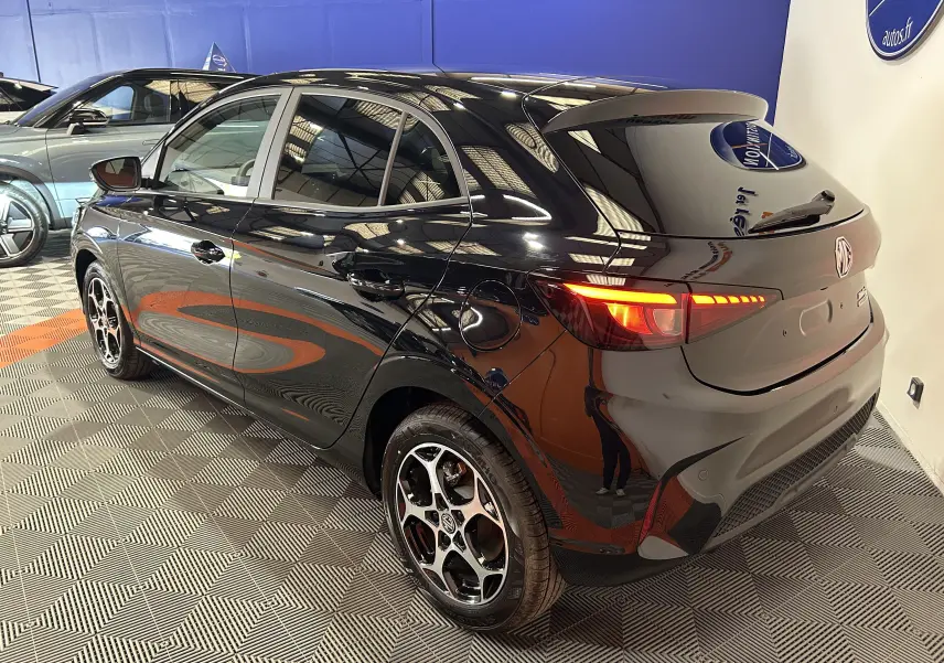 Vue 3/4 arrière droite d'une MG3 Hybrid+ 195 Luxury Pebble Black avec feux arrière allumés dans un showroom.