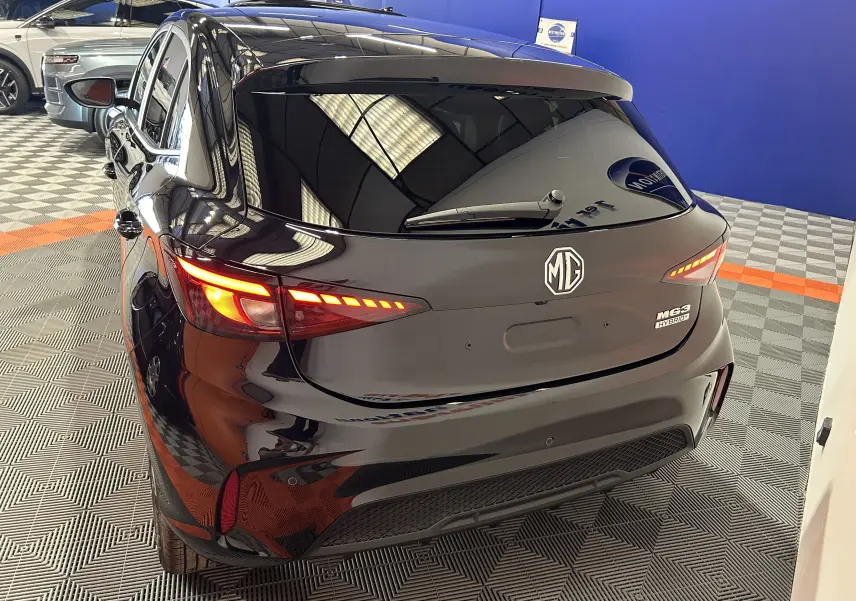 Vue 3/4 arrière droite d'une MG3 Hybrid+ 195 Luxury Pebble Black avec feux arrière allumés dans un showroom.