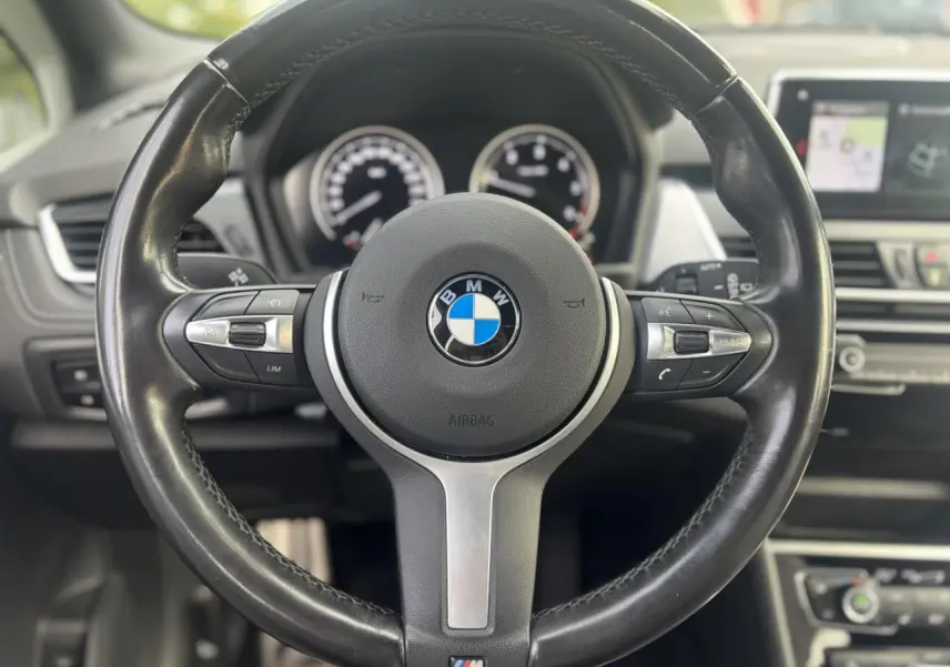 Vue rapprochée du volant cuir M noir de la BMW Série 2 Active Tourer 218dA 2020 avec tableau de bord et écran GPS en arrière-plan.