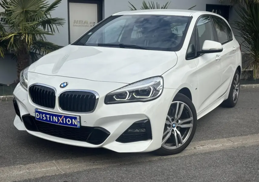 BMW Série 2 Active Tourer blanc vue 3/4 avant droit avec jantes alliage 18 pouces et phares LED allumés.