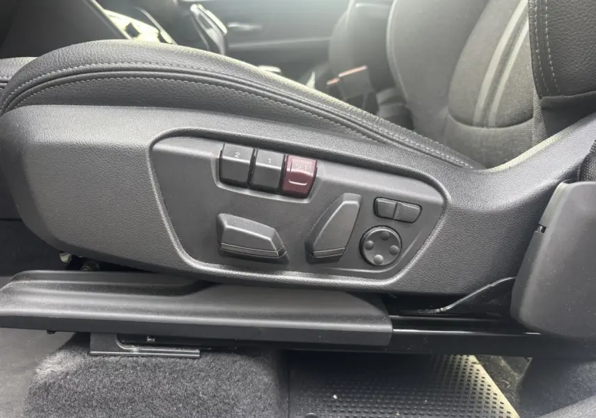 Gros plan sur les commandes électriques du siège conducteur noir dans une BMW Série 2 Active Tourer blanche.