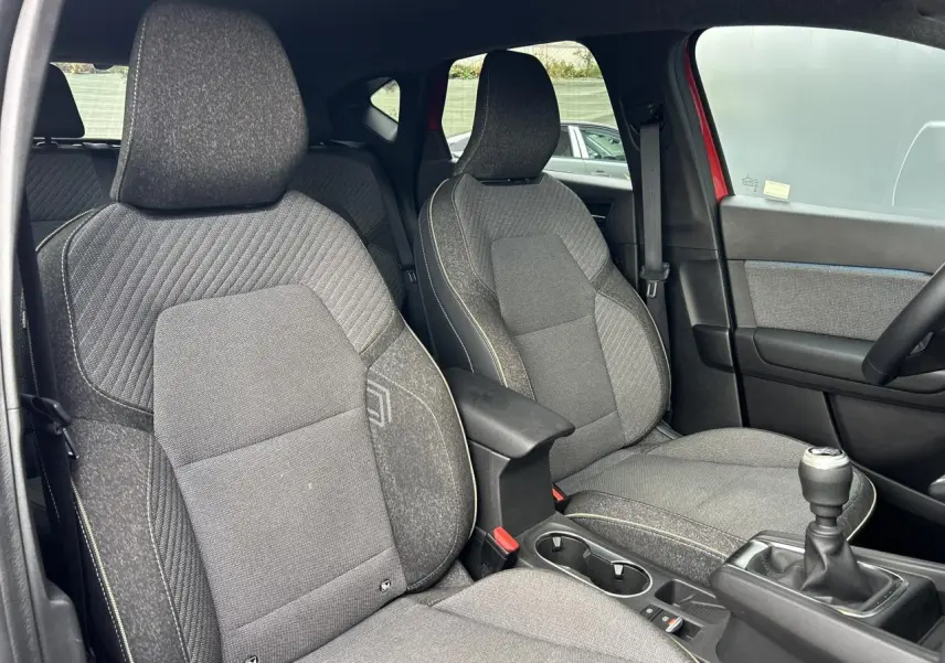 Vue intérieure côté conducteur du Renault Captur 2025, sièges gris avec coutures jaunes et levier de vitesse manuel.