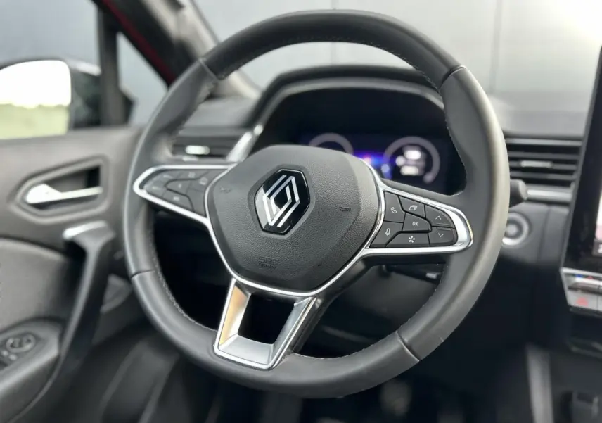 Vue rapprochée du volant noir du Renault Captur 2025 avec commandes intégrées et tableau de bord numérique flou en arrière-plan.