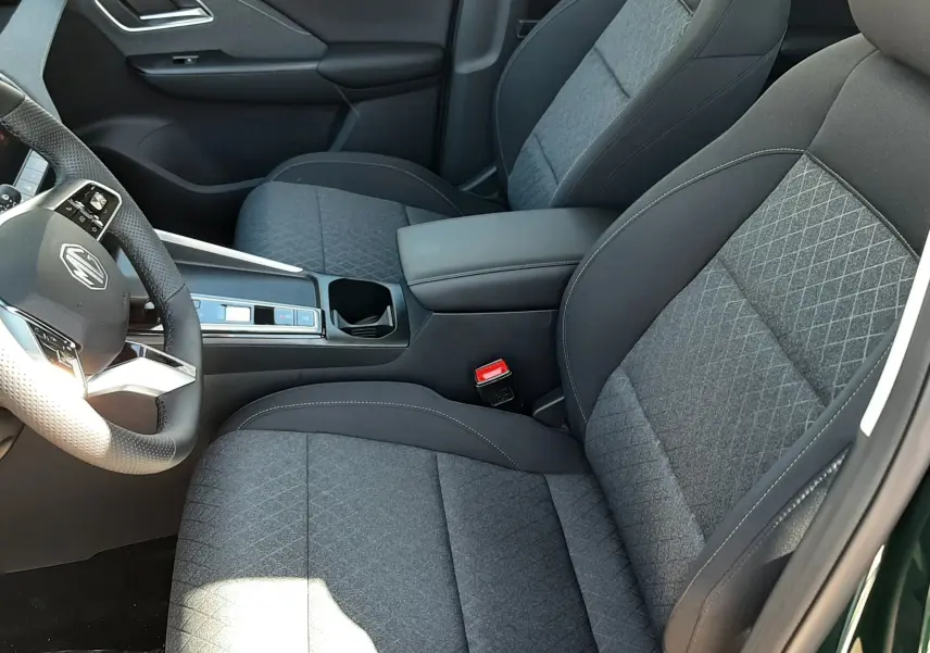 Vue intérieure côté conducteur du MG Motor ZS 1.5 Hybrid+ 2026, sièges tissu gris avec coutures contrastées.