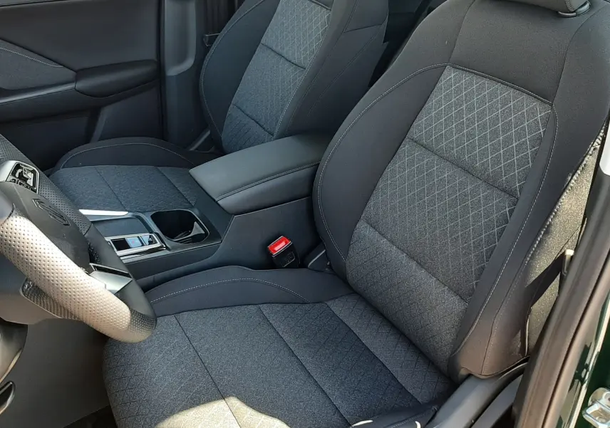 Vue intérieure côté conducteur du MG ZS 1.5 Hybrid+ 2026, sièges tissu gris avec surpiqûres losanges et accoudoir central.